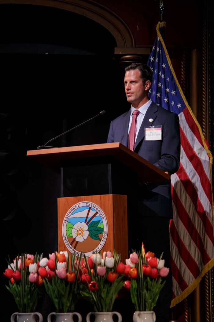 Speaker at a wooden podium beside an American flag, red tulips in the foreground