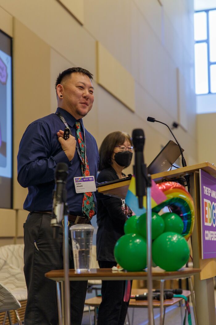 Smiling presenter with a slide clicker beside green balloons at the conference