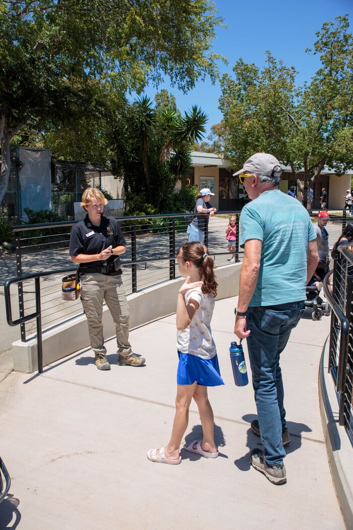 Zookeeper talking with a man and his daughter along a sunny path