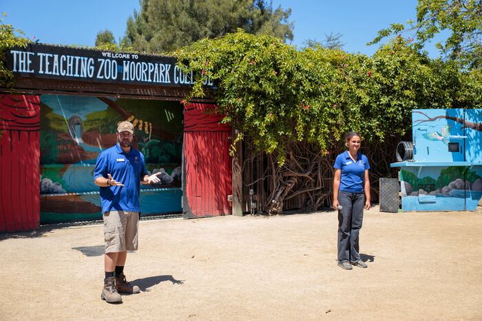 Two zoo staff welcoming guests at the colorful Teaching Zoo entrance