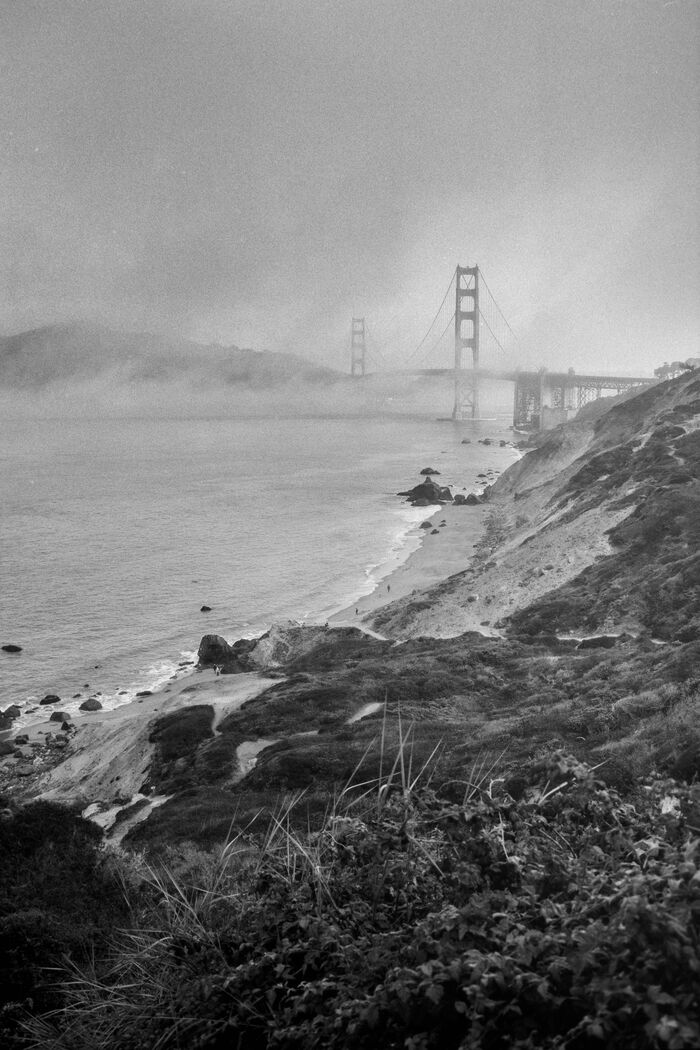 Golden Gate Bridge in fog above a rocky coastline, black and white