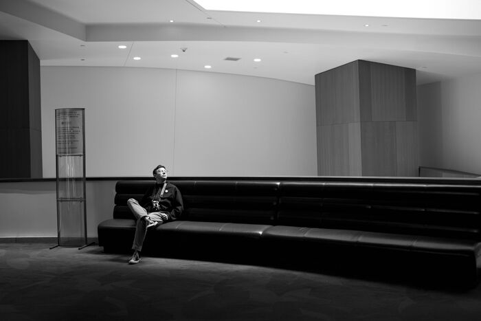 Man reclining on a long bench in a minimal lobby, black and white