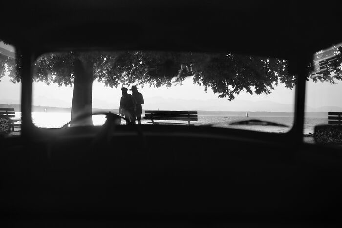 Two silhouetted figures framed by a dark pavilion overlooking the water