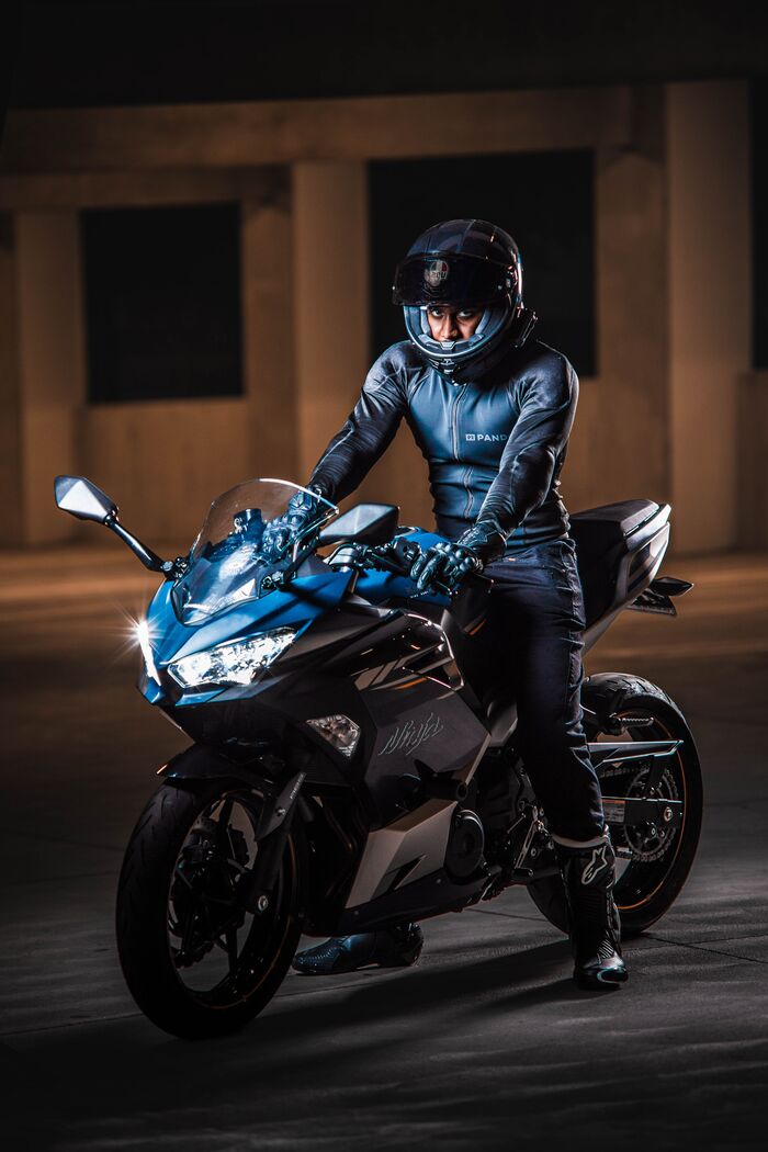 Rider in helmet and leathers on a blue sport motorcycle, lit in a dark barn
