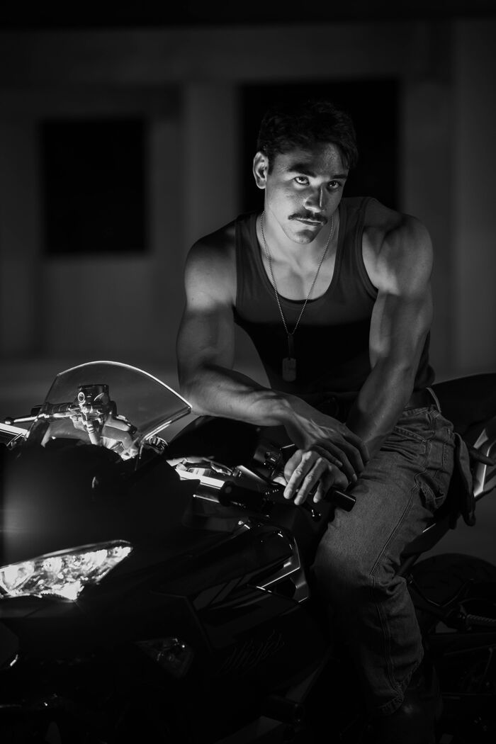 Black and white portrait of a man in a tank top leaning on a motorcycle