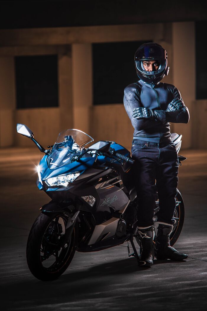 Rider in helmet and blue leathers standing beside a sport motorcycle in a dark barn
