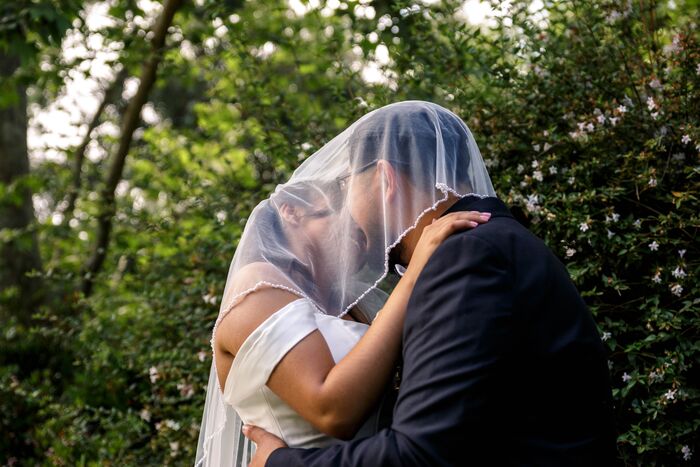 Bride and groom embracing under her veil in a garden