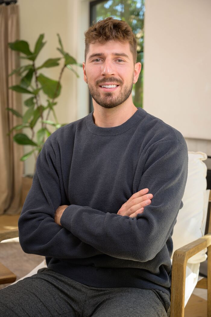 Man in a charcoal sweater seated with arms crossed, smiling
