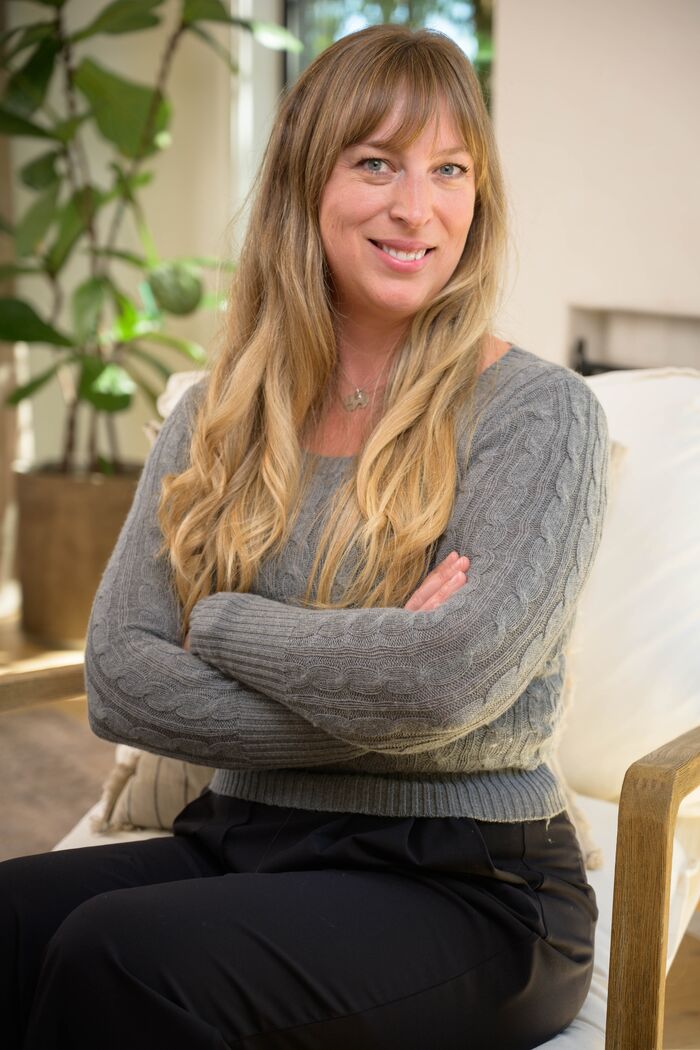 Woman in a grey sweater seated with arms crossed, smiling