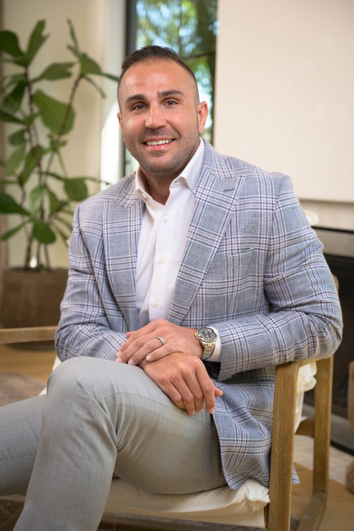 Man in a light plaid blazer and open-collar shirt seated with hands clasped
